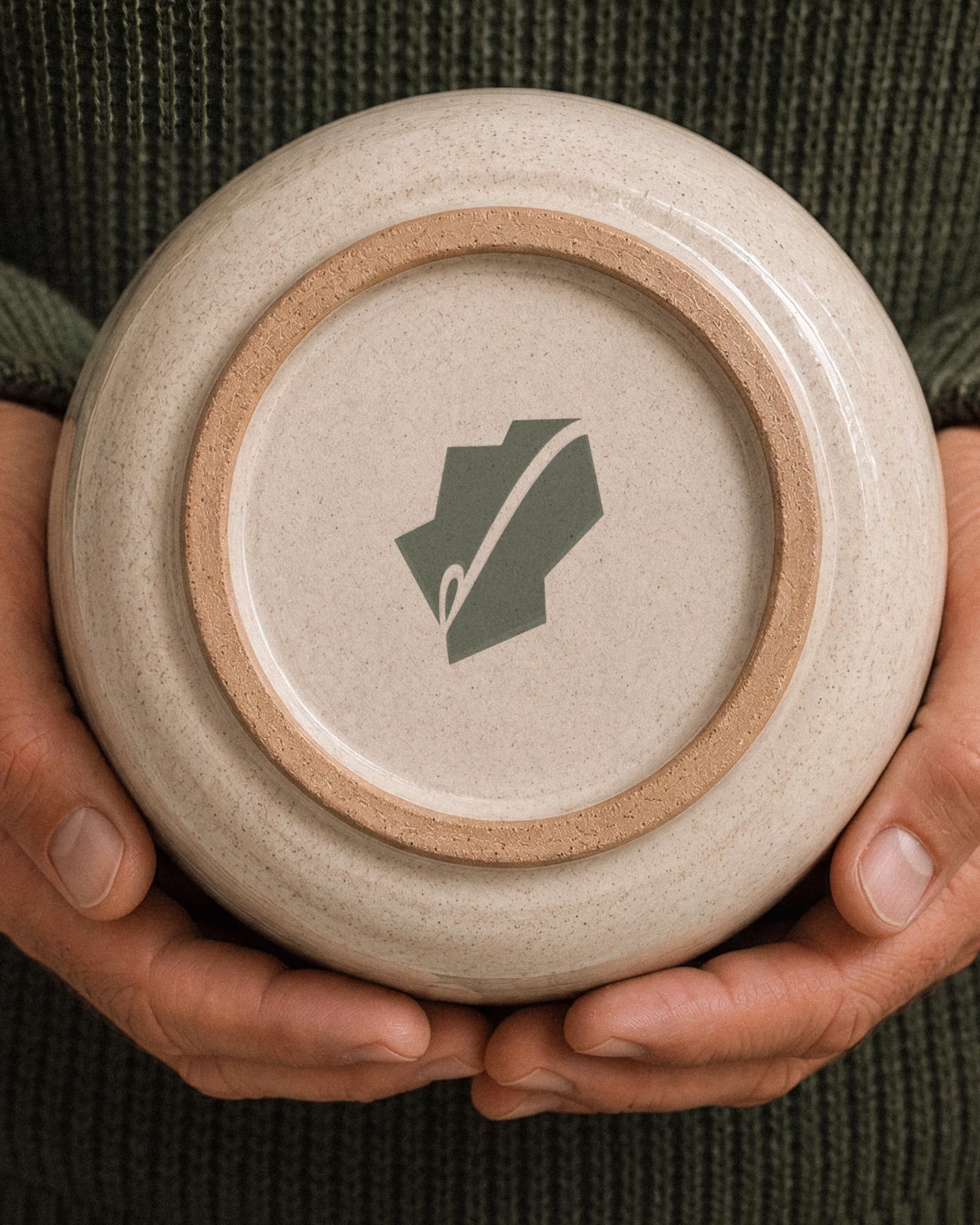 Hands holding a ceramic pot with the Patch symbol embossed on the base