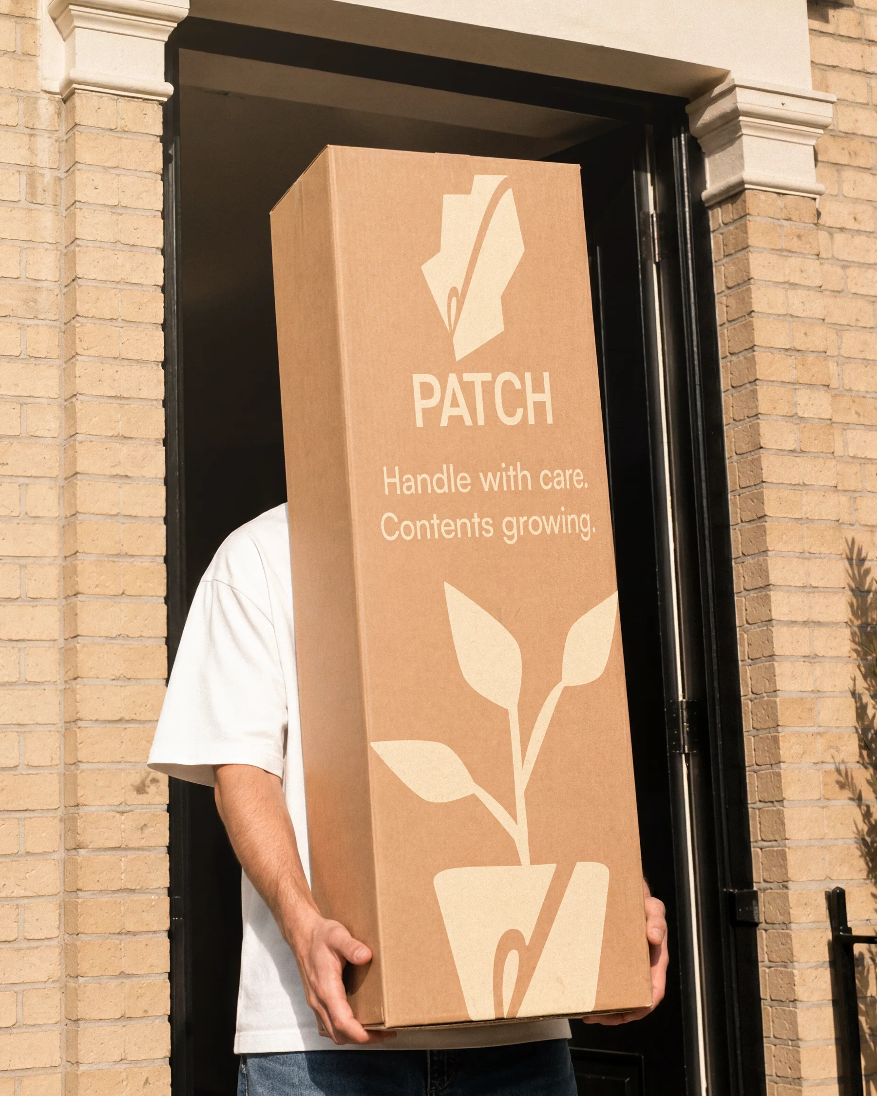 Tall Patch delivery box carried through a front door, printed with the plant illustration and the line Handle with care, contents growing